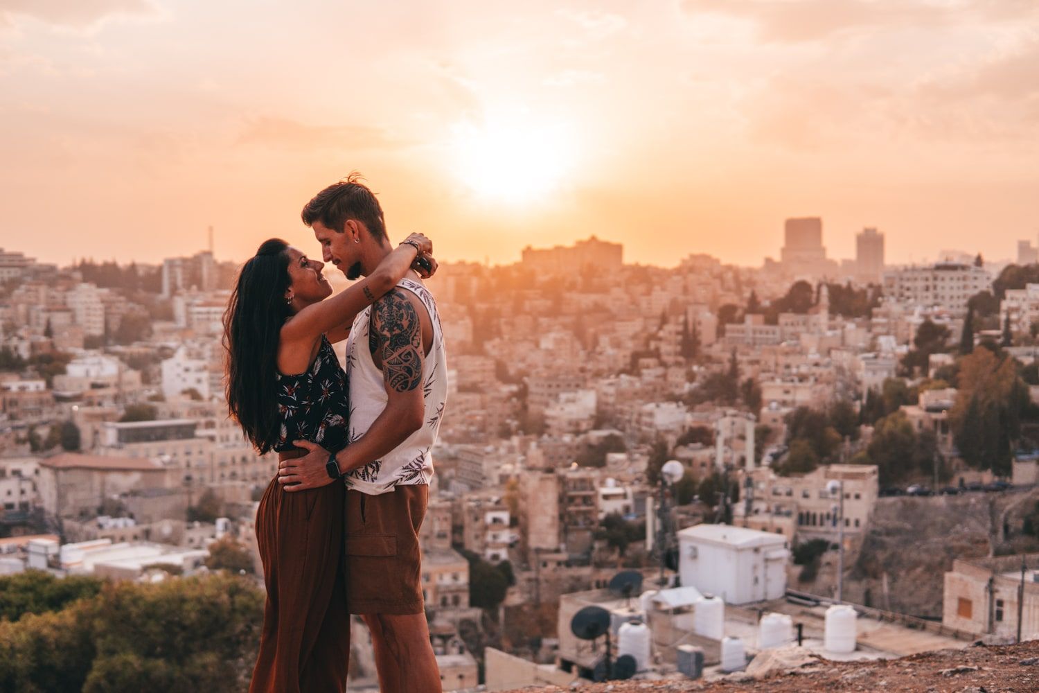 Pareja abrazándose, desde lo alto de la Ciudadela de Amán y con la ciudad y el sol poniéndose al fondo.