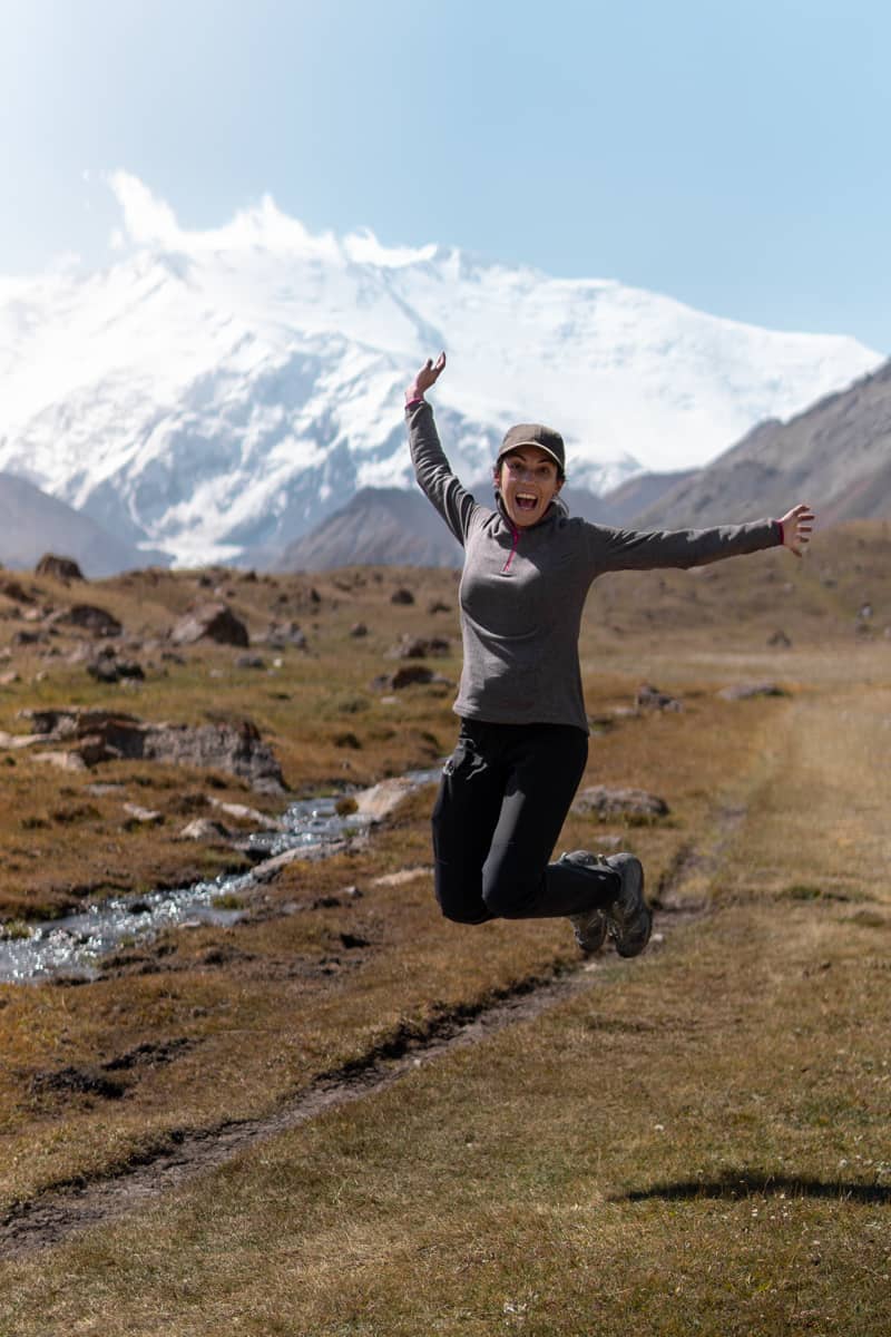 Chica saltando en medio del campo, y con el Pico Lenin de fondo, al sur de Kirguistán.