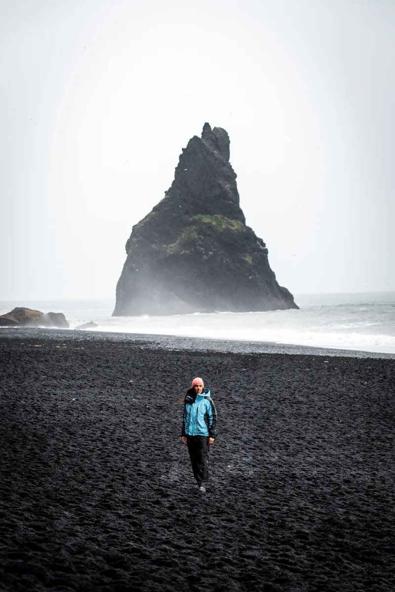 Chica con un abrigo azul claro, de pie en la playa negra de Reynisfjara, uno de los puntos de la ruta por Islandia en 10 días