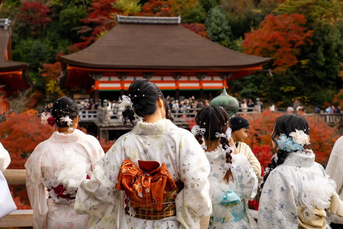 chicas japonesas de espaldas con kimonos tradicionales y templo de fondo durante el momiji