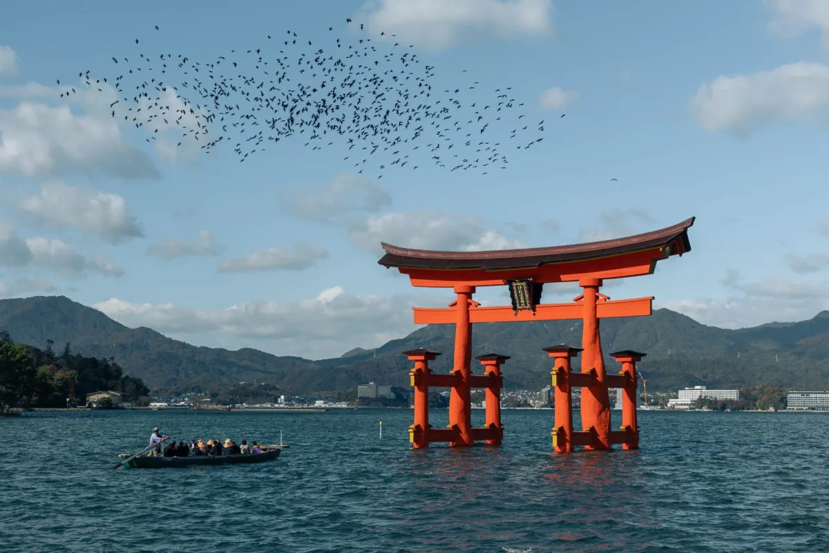 Torii en Isla de Miyajima con pájaros volando y una barca con personas en el mar