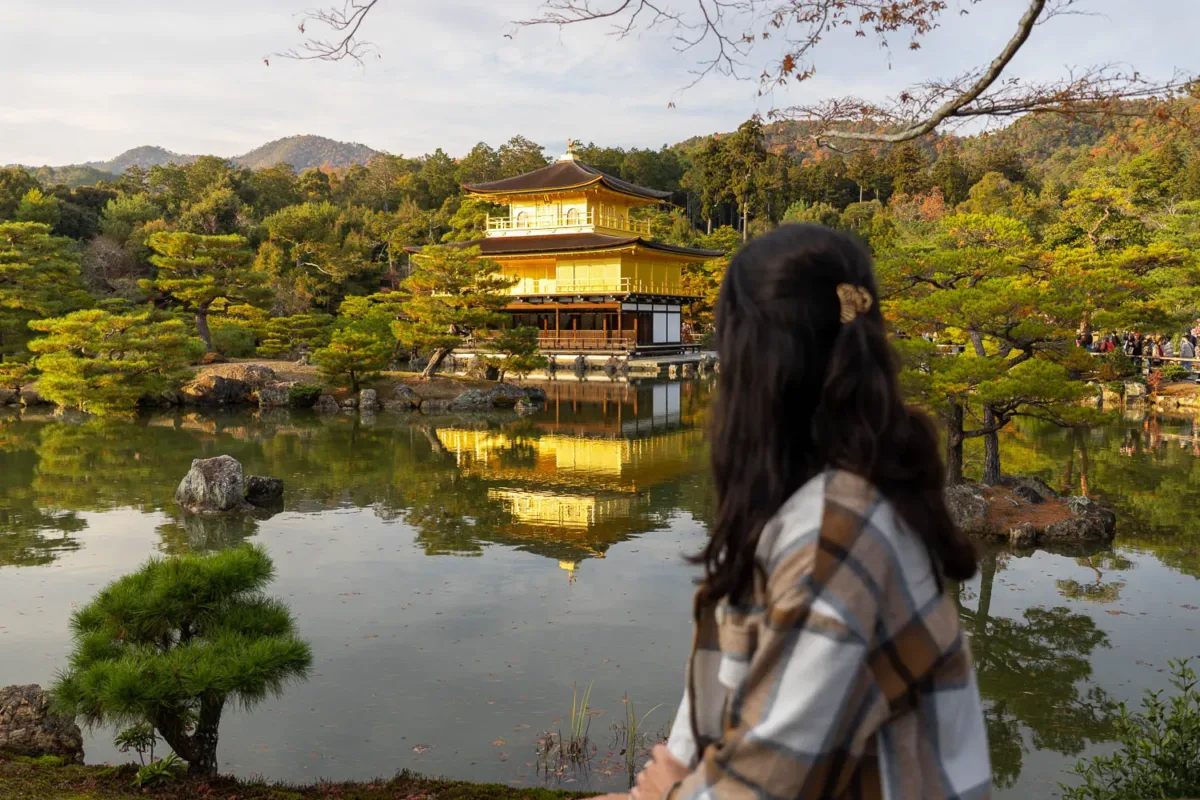 Silvia de espaldas contemplando el Pabellón Dorado o templo Kinkaku-ji y reflejo en el estanque con luz de atardecer durante su visita a Kioto en dos días