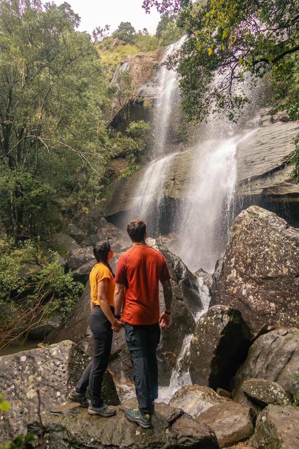 Pareja cogidos de la mano, mirando hacia una cascada en uno de los trekkings de Drakensberg, en Sudáfrica.