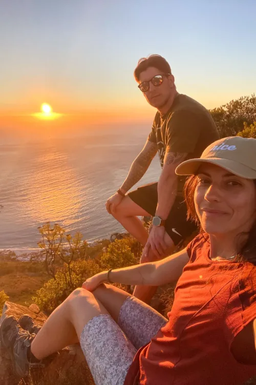 Atardecer en el mar desde la cima de una colina con pareja mirando a cámara.
