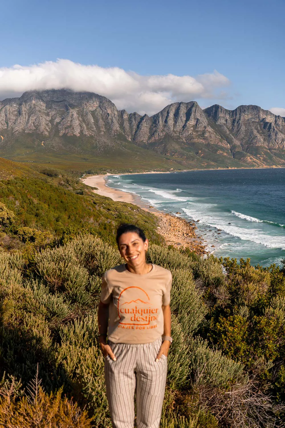 Chica con un paisaje de una playa de agua clara y montañas detrás, en la Garden Route, uno de los lugares que ver en una ruta por Sudáfrica en 20 días.