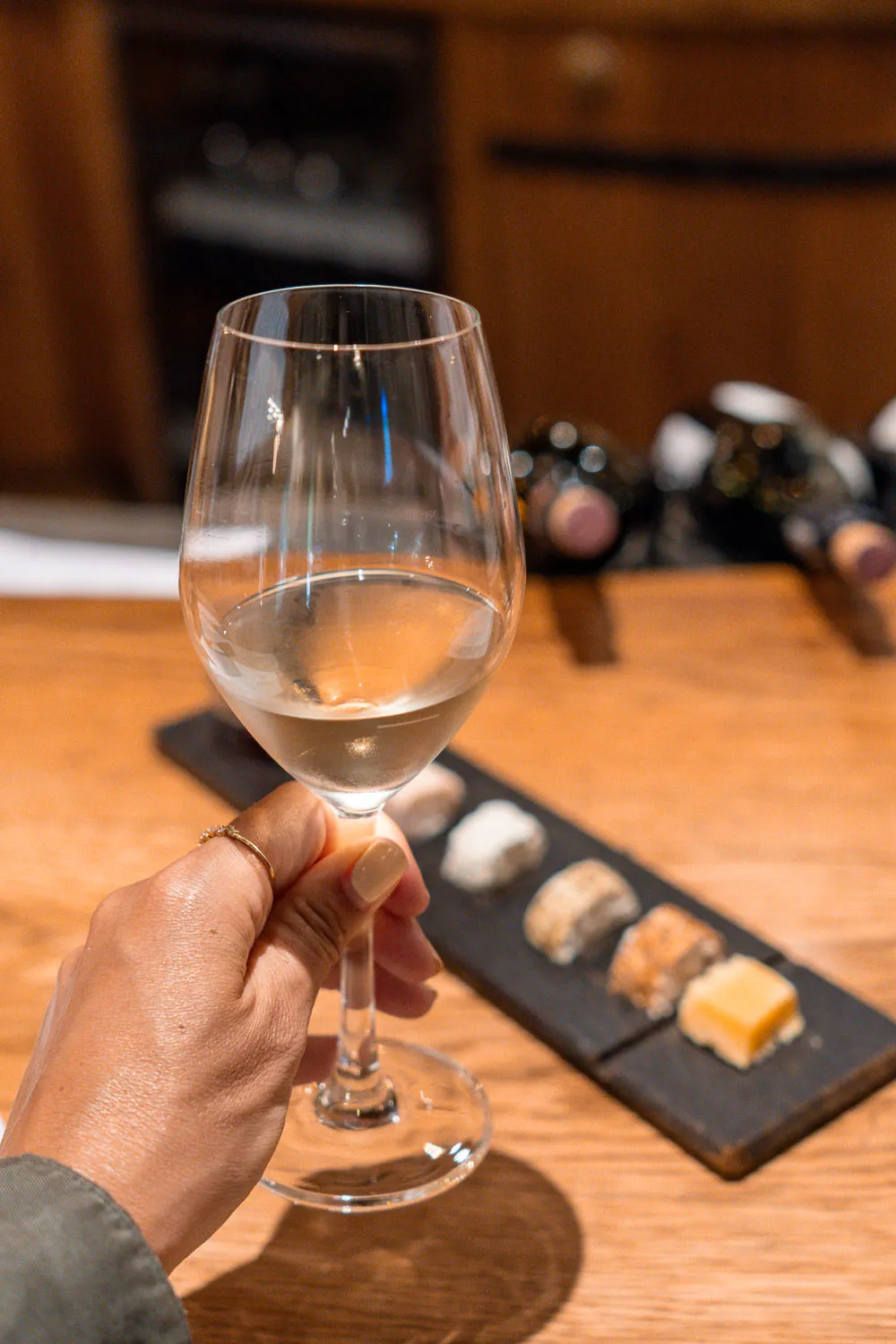 Copa de vino blanco, más en detalle con una tabla de quesos de fondo.