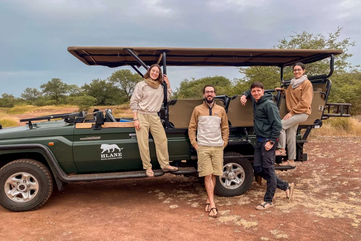 Grupo de amigos posando delante de un vehículo de safari en la sabana africana.