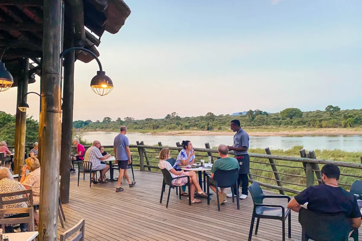 Terraza, con gente sentada del campamento Lower Sabie, con el río de fondo y las vistas al Parque Nacional Kruger.