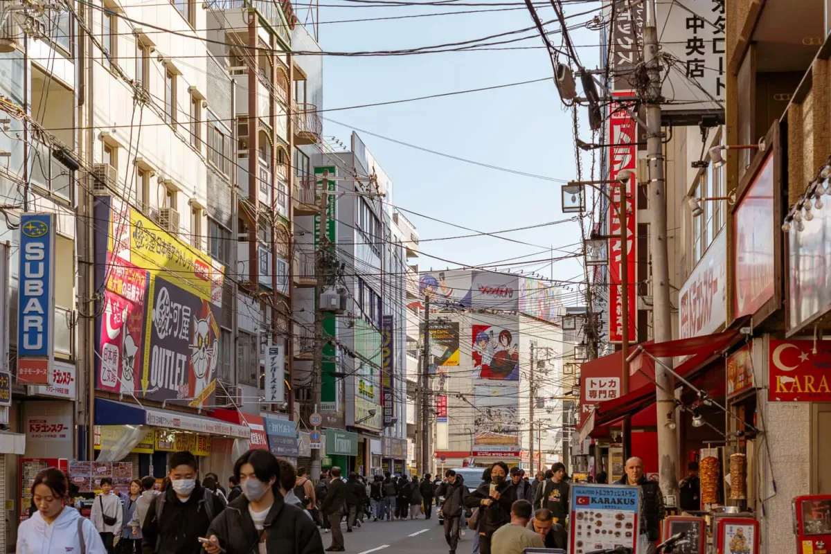 Calle con gente, cables cruzando de lado a lado entre edificios y cárteles de animes en barrio Nipponbashi, uno de los barrios que ver en Osaka en 2 días