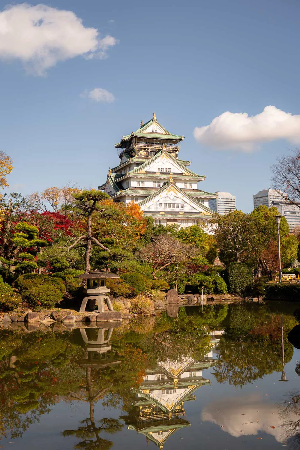 Castillo tradicional japonés en Osaka con jardín y reflejo en lago.